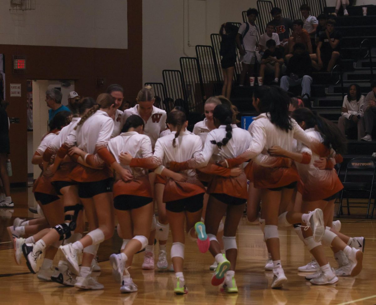 Kicking their feet in unison, the varsity volleyball team hypes each other up immediately before the game. The group huddle is a tradition before every game, establishing camaraderie.