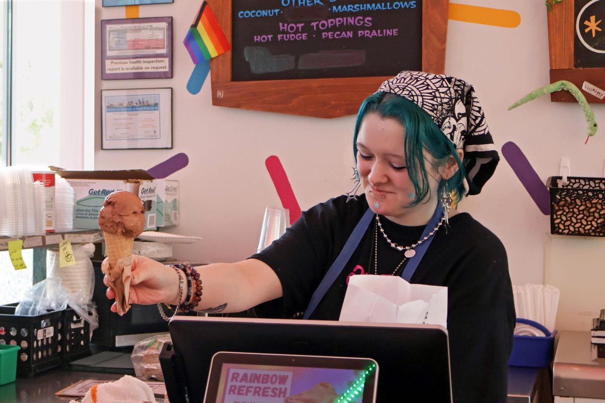 Holding out a dark chocolate cone, an Amy's Ice Cream employee serves a customer. From the start of the ice cream shop in 1984, cultivating an open-minded community and delivering joy has been one of their primary goals, reflected by their slogan: "Making People’s Day”.