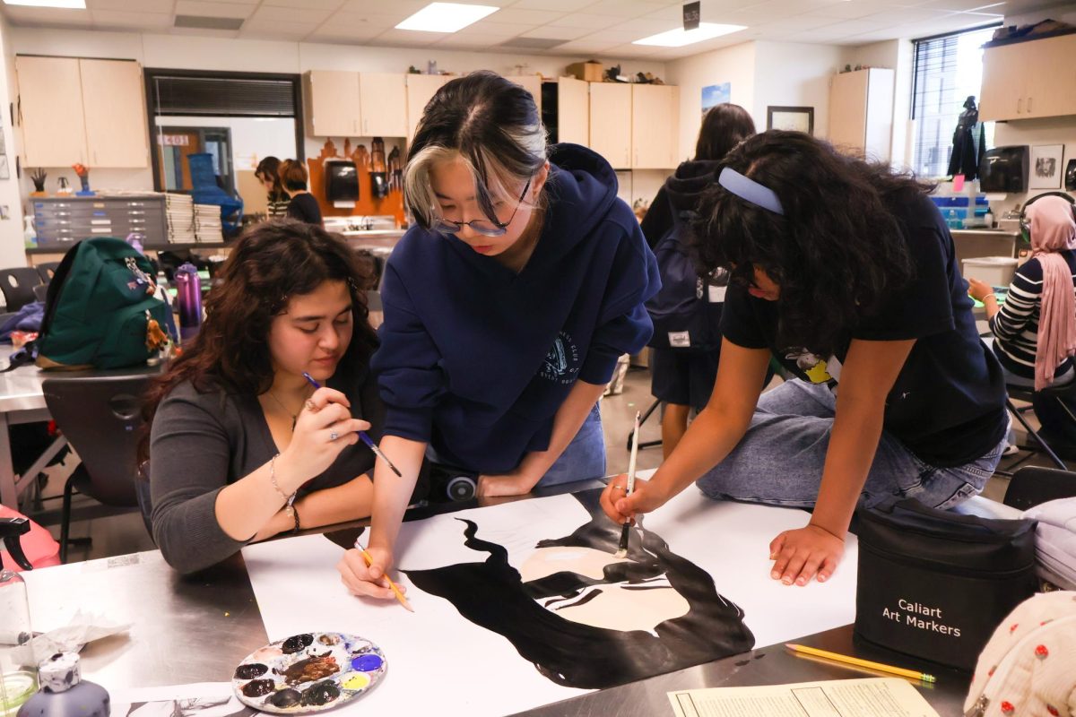 Intensely concentrated, seniors Ari June, Christine Kim, and Sahana Suryanarayan collectively paint a portrait of Charli XCX's face. While painting, they shared stories about past experiences and bonded over similar interests in music. "I've definitely grown as a collaborator because in NAHS [National Art Honor Society], you're all growing together as artists and collaborators," Suryanarayan said. "The portrait helped me make room for others while painting."