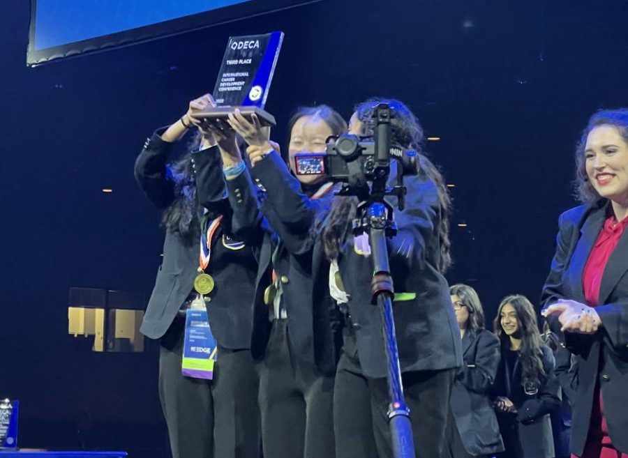 Beaming, Shrishti Mahajan '25, Bailey Zhang '25, and Shivani Kondubhatla '25 hold their 3rd place trophy in the air at the DECA International Conference awards ceremony. The team of sophomores won in the Hospitality and Tourism Operations Research event.