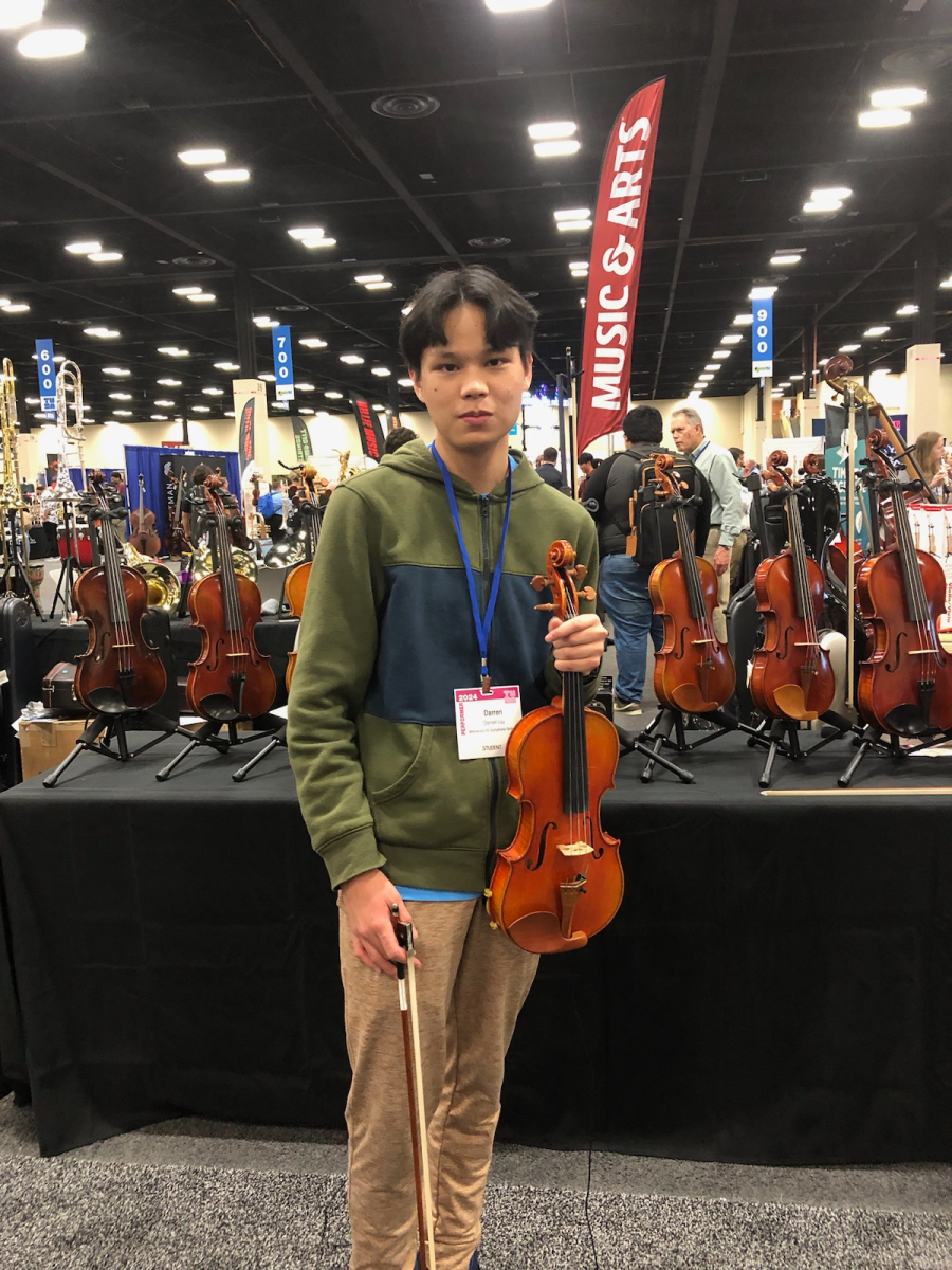 Violinist Darren Liu '24 stands in front of a row of violins on display at the Texas Music Educators Association (TMEA) convention. Westwood's Symphony Orchestra was invited to TMEA for an honors recital because they were recognized as the best orchestra in Texas.